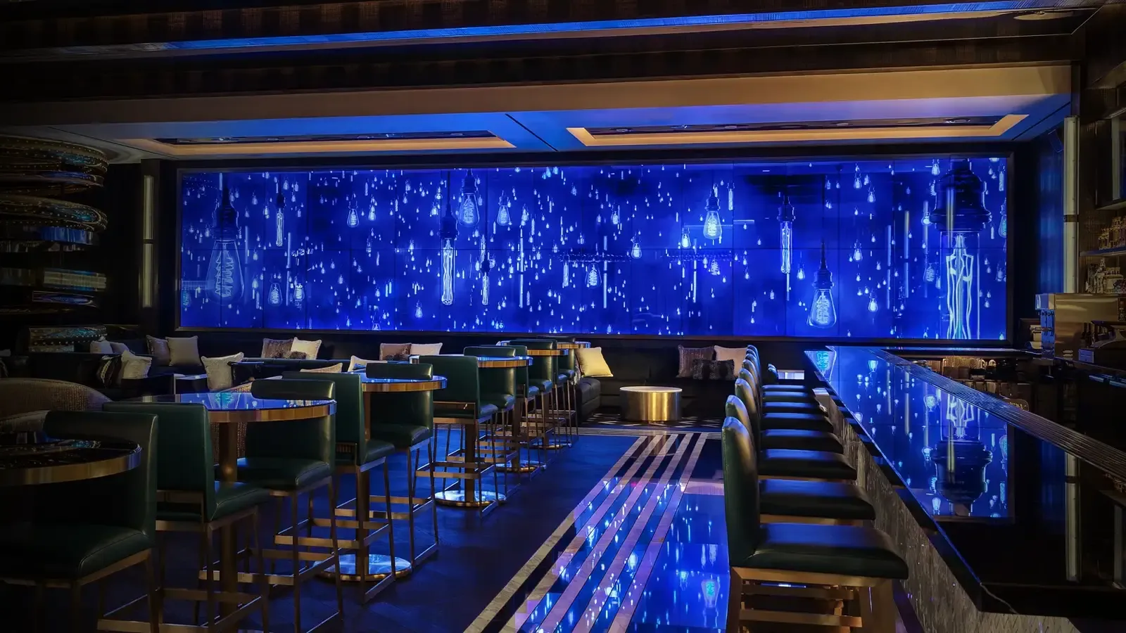 Floor-to-ceiling blue LED video wall glowing behind the counter of an upscale bar