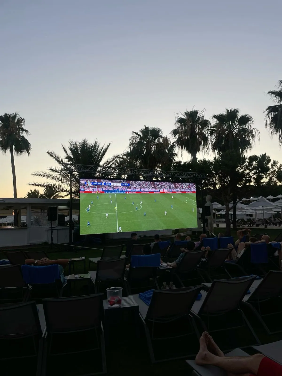 Crowd watching a live match on an outdoor LED screen as daylight fades to dusk